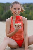 Charming teenage cutie enjoys getting naked and eating a watermelon outside in the dunes.