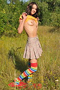 Cute teen in long striped socks taking off her clothes outdoors in the field